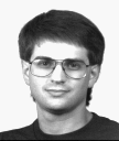 A man with glasses looking into camera, head tilted slightly.