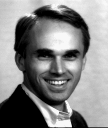 A man with parted hair looking directly into the camera, smiling.