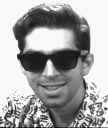 A man in a patterned shirt, smiling and wearing glasses.